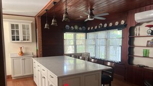 A kitchen with a central island, wooden cabinets, a ceiling fan, and a window with lace curtains.