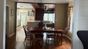 A dining area with a wooden table and chairs, a chandelier, and a view into the kitchen.