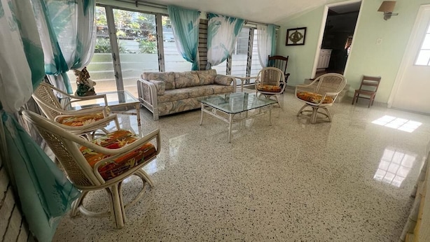 A spacious living room with a sofa, two armchairs, a glass coffee table, and a dining table.