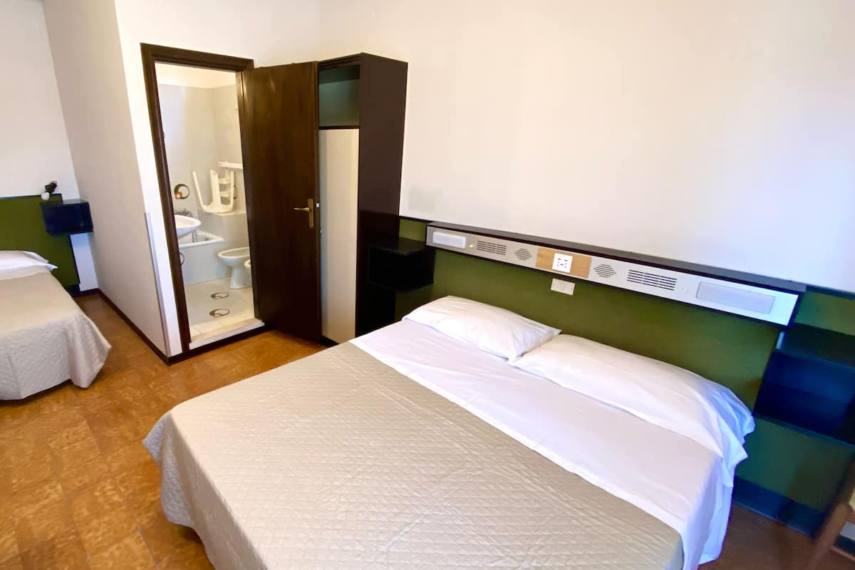 A hotel room with a large bed, a smaller bed, a wardrobe, a mirror, and a bathroom visible through an open door.