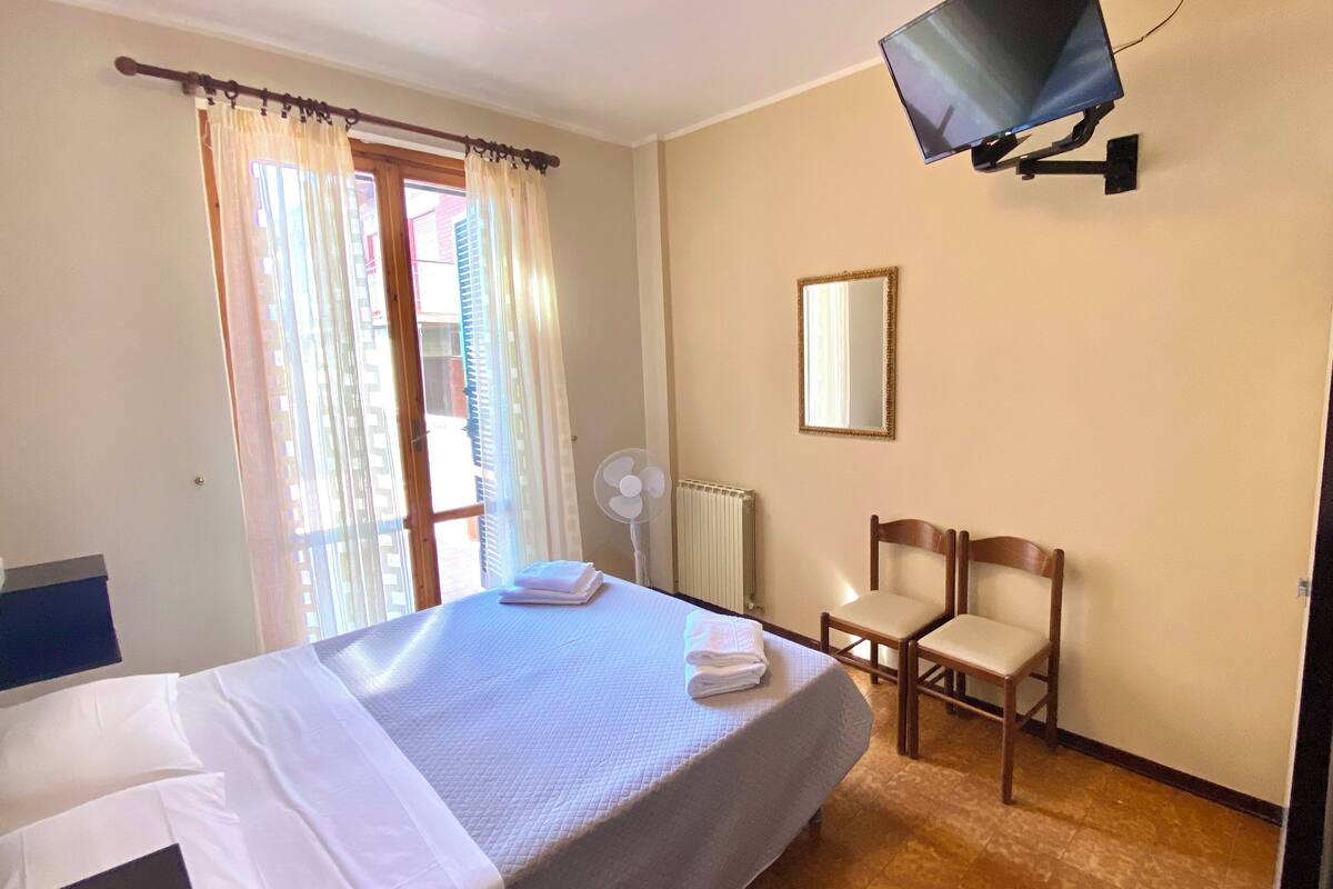 A hotel room with a bed, a chair, a television mounted on the wall, and a window with curtains.