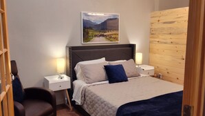 Ein Schlafzimmer mit einem Bett, zwei Nachttischen inklusive Lampen, einem Sessel, einer Holzwandverkleidung und einem gerahmten Bild an der Wand.