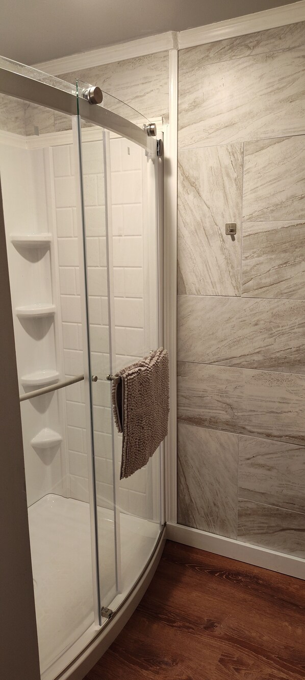 Une douche fermée par des parois en verre, avec des carreaux blancs et une serviette beige accrochée à la porte.