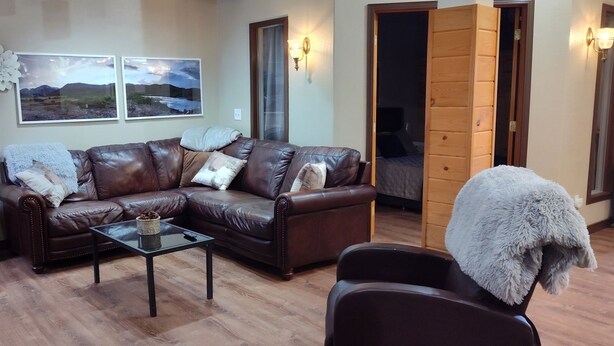 Ein Wohnzimmer mit braunem Ledersofa, einem Glastisch und Holzboden. Zwei Bilderrahmen sind an der Wand befestigt und eine hohe Stehlampe steht im Raum.
