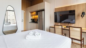 Een hotelkamer met een bed, een bureau met twee stoelen, een kitchenette, een grote spiegel en een televisie aan de muur.