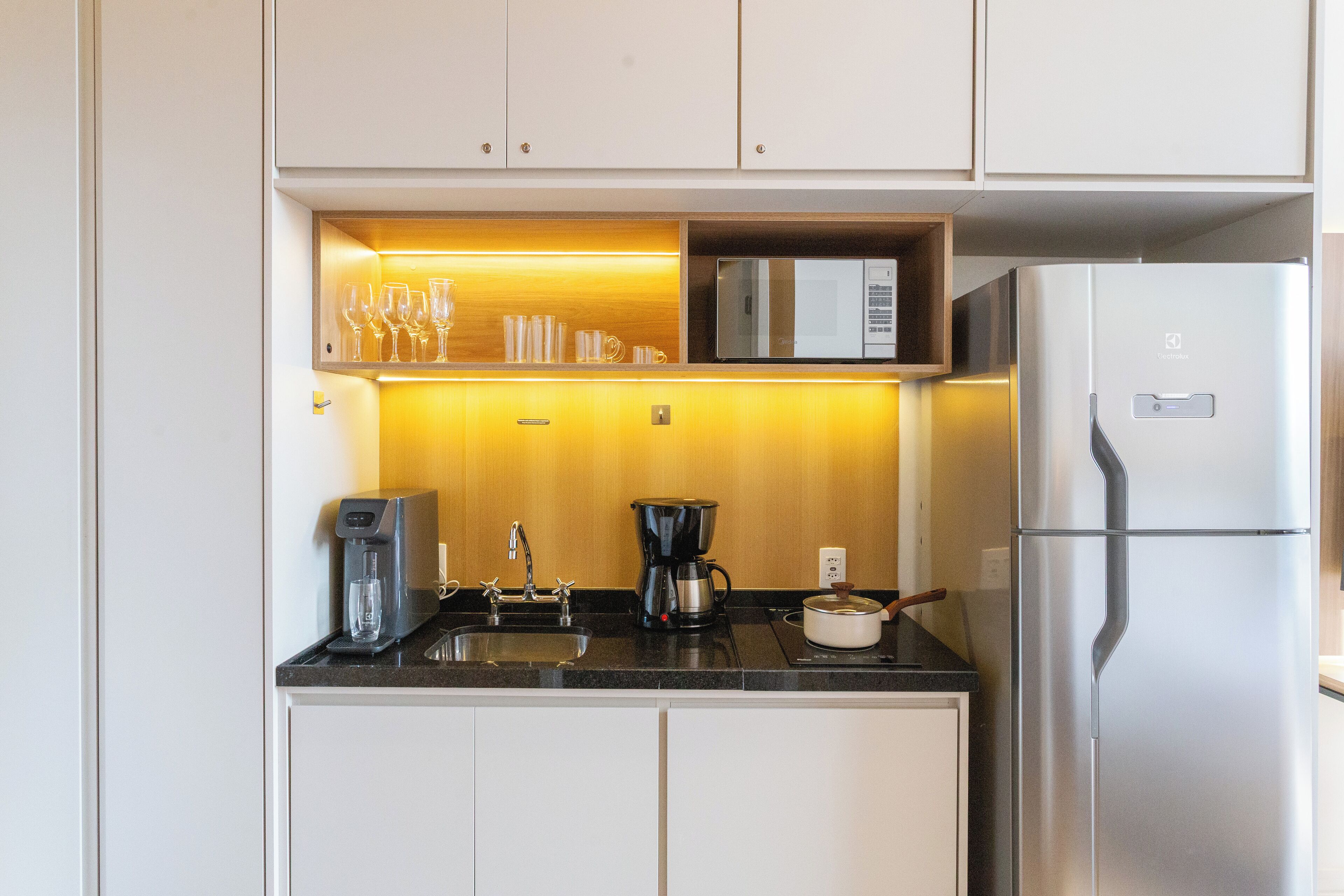 A compact kitchen with a built-in microwave, coffee maker, and a refrigerator.