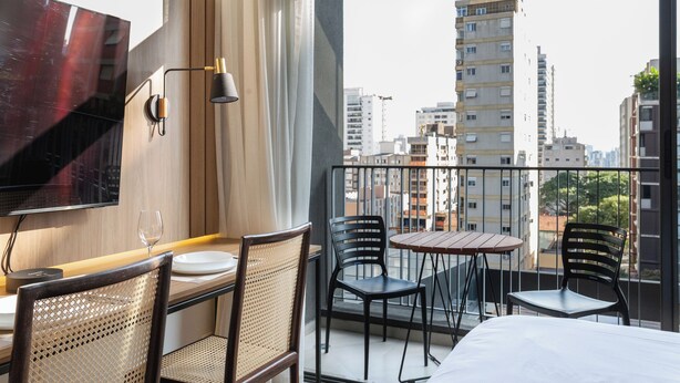 Hotelkamer met balkon, televisie, eethoek met stoelen en tafel, en uitzicht op de stadslijn.