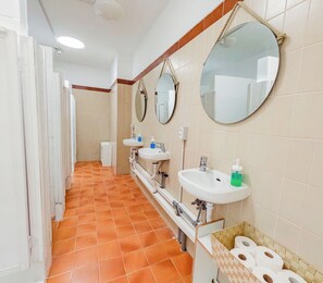 A public restroom with multiple sinks, mirrors, and a toilet paper dispenser. - Las Eras Nest Hostel (Arico)
