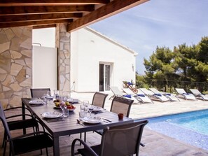 An outdoor dining area with a poolside view, stone walls, and lounge chairs.