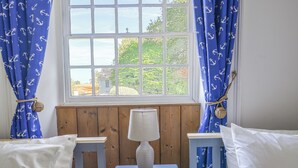 Ein Zimmer mit Fenster, Holzvertäfelung, einem kleinen Tisch mit Lampe und zwei weißen Betten mit passenden Kissen.