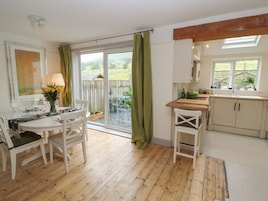 A dining area with a table and chairs, a kitchen with cabinets and a sink, and a sliding glass door leading to a garden.
