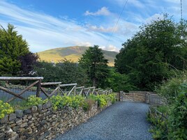 A stone pathway leading to a wooden gate, surrounded by greenery and a stone wall.