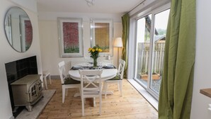 A dining area with a round table set for four, white chairs, a small stove, and artwork on the walls. - Beech Croft (Keswick)