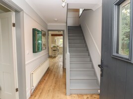 Un pasillo con piso de madera, una escalera gris y una ventana a la derecha.
