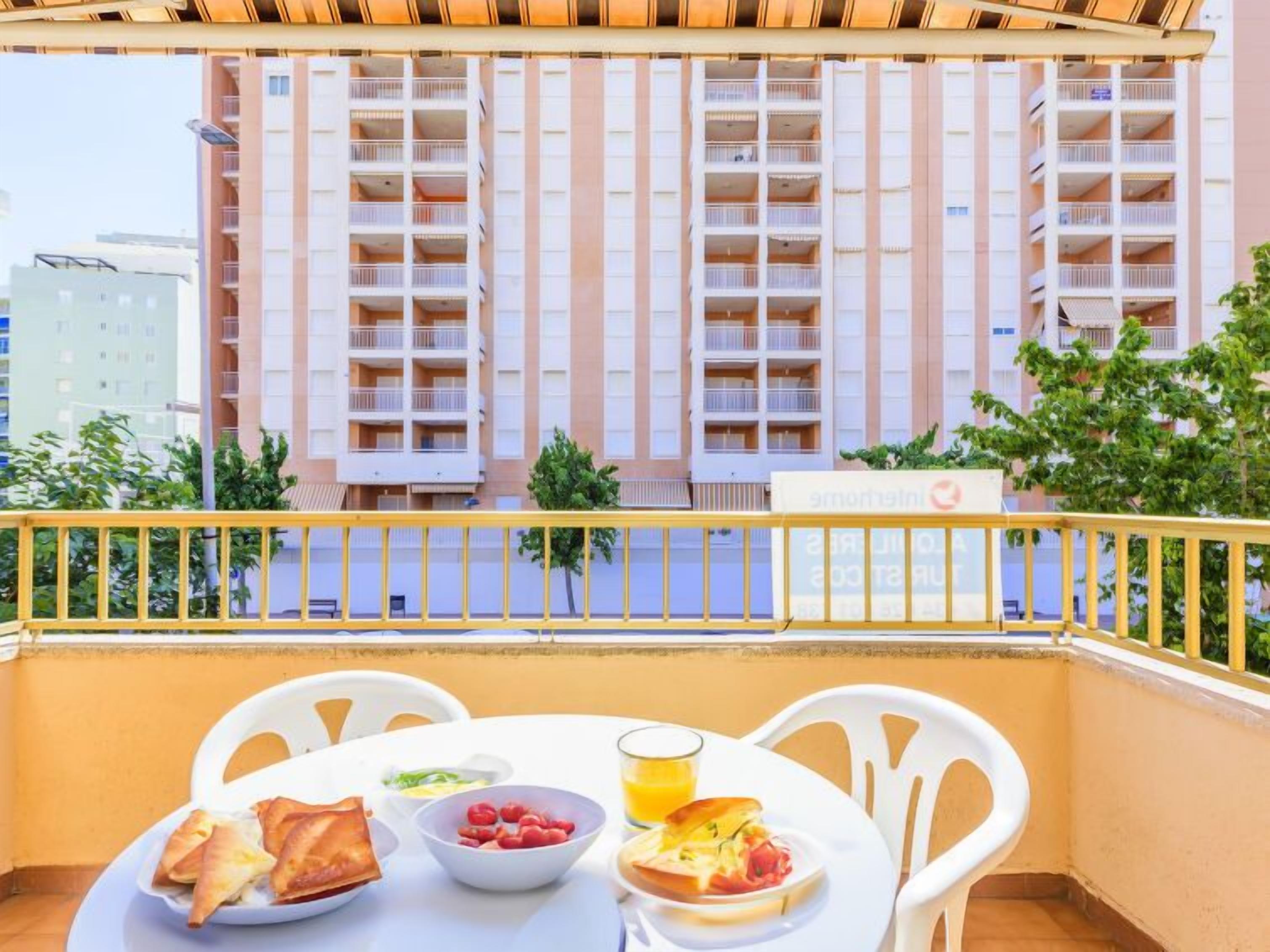 Ein Balkon mit einem Frühstückstisch, mit Blick auf ein Gebäude mit mehreren Balkonen.