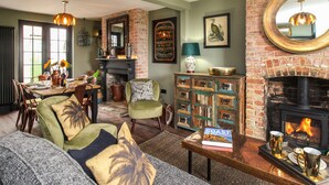 Un salon chaleureux avec une cheminée, un coin repas avec une table dressée pour quatre personnes, et un espace salon confortable avec un canapé et des fauteuils.