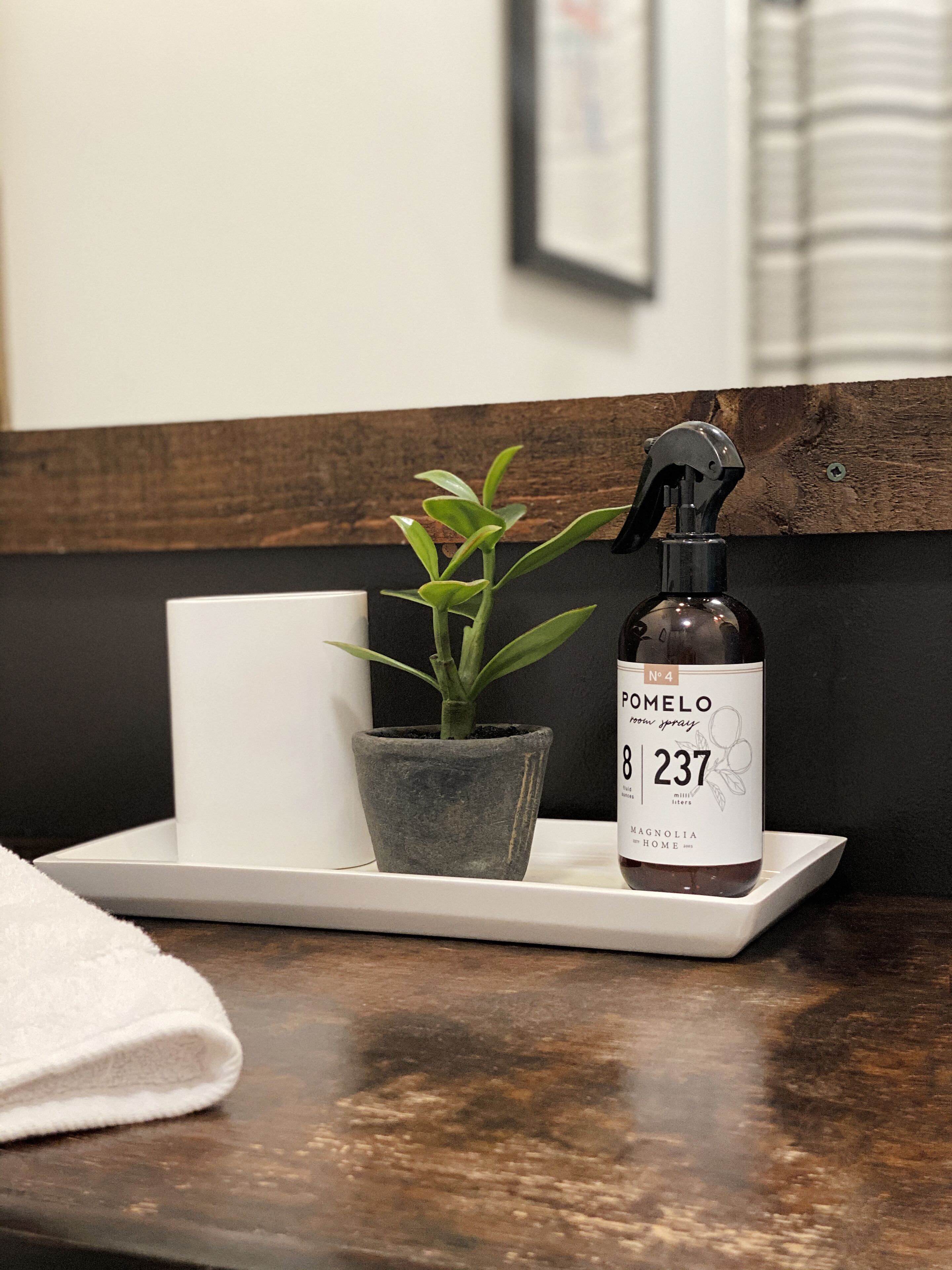 A bathroom counter with a potted plant, a bottle of Pomelo room spray, and a white tray.