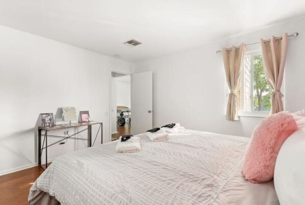 Un dormitorio con cama, escritorio y ventana con cortinas.