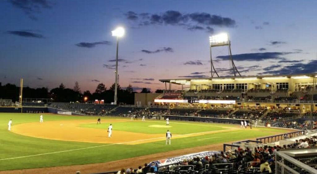 A baseball stadium at dusk with a well-lit field and seating areas.