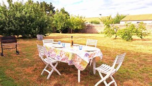 An outdoor dining area with a round table covered with a floral tablecloth, surrounded by white chairs. - La Maison du Verger - 13km from the beach (Sainte-Foy)