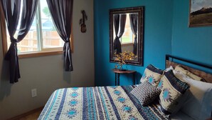 A bedroom with a bed, a nightstand, a mirror, and a window with curtains.