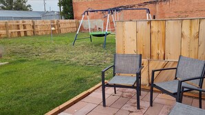 A backyard patio with two chairs and a swing set.