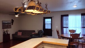 A living room with a sofa, a dining table with chairs, a ceiling fan, and a decorative light fixture.