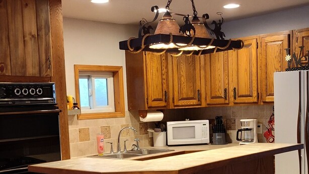 A kitchen with wooden cabinets, a central island with stools, a microwave, and a refrigerator.