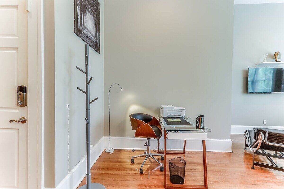 A room with a desk, chair, lamp, and a coat rack.