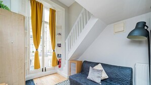A cozy room with a blue sofa, a patterned rug, a staircase, and a lamp. - Studio in Notting Hill (London)