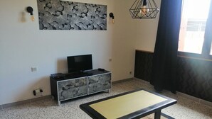 A living room with a TV on a cabinet, a coffee table, a patterned wall, and a hanging light fixture.