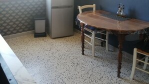 A compact kitchen with a refrigerator, a dining table with chairs, and a window with blinds.