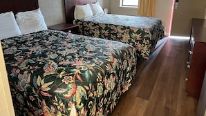 A hotel room with two beds, a window with curtains, a wooden dresser, and a door.