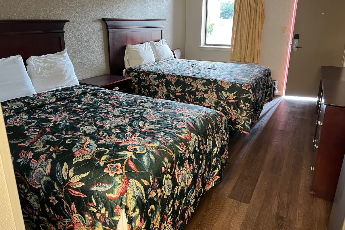 A hotel room with two beds, a window with curtains, a wooden dresser, and a door.