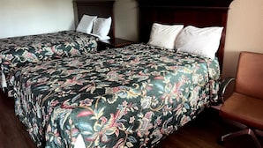 Two twin beds with floral bedding, a wooden headboard, and a brown leather chair in a hotel room.