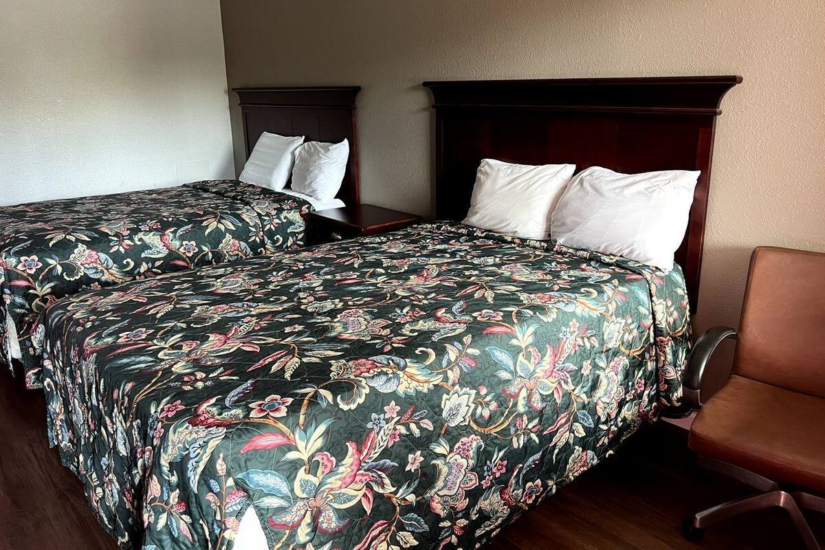 Two twin beds with floral bedding, a wooden headboard, and a brown leather chair in a hotel room.