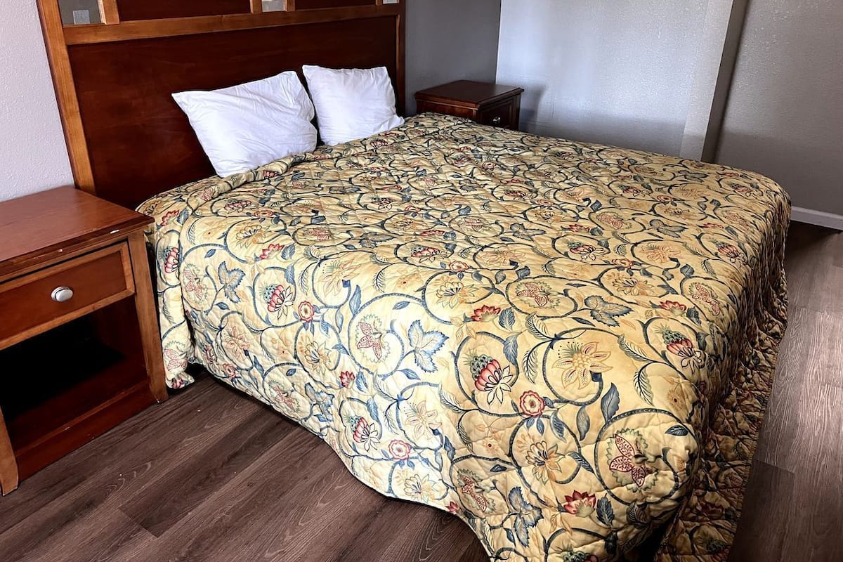 A bedroom with a wooden headboard, a floral-patterned bedspread, two bedside tables, and a nightstand.