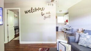 Sala de estar com ventilador de teto, sofá, mesa de centro e parede com a placa 'welcome be our guest'.