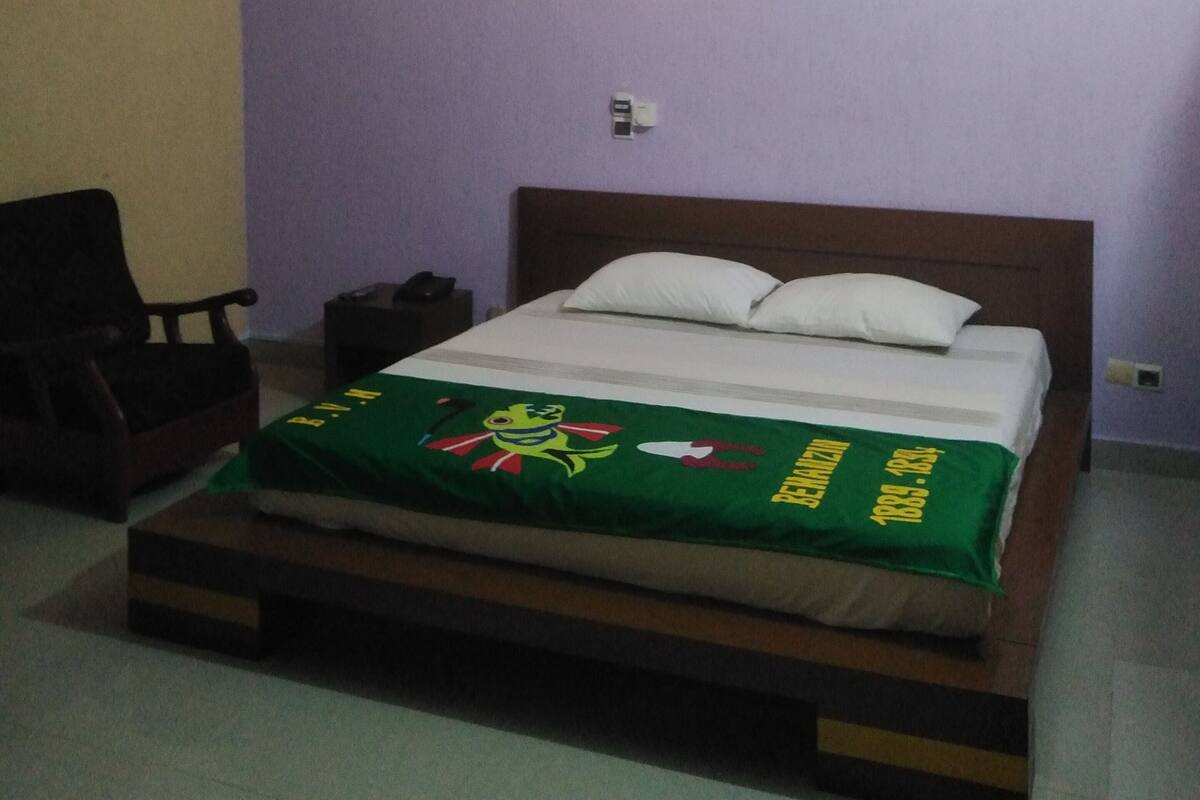 Un dormitorio con cama, ventilador de techo, lámpara de pared y una silla.