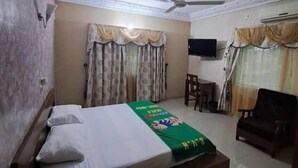 Habitación de hotel con cama, escritorio, silla, ventilador de techo y televisión.