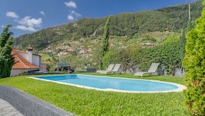 A swimming pool surrounded by well-maintained grass, with a view of a hillside village in the background. - Villa Paixão (Machico)