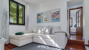 A modern living room with a white sectional sofa, a grey rug, and three framed artworks on the wall. - Villa Paixão (Machico)