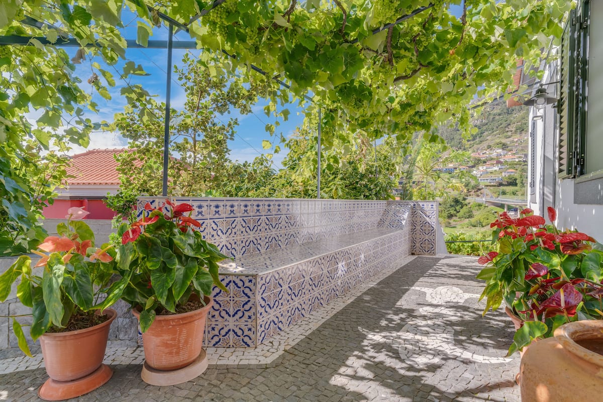 A tiled bench with potted plants, a tiled wall, and a view of a hillside with houses.