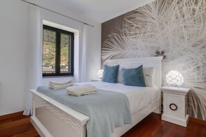 A bedroom with a large bed, a nightstand, a window with curtains, and a wall with a feather-like design.