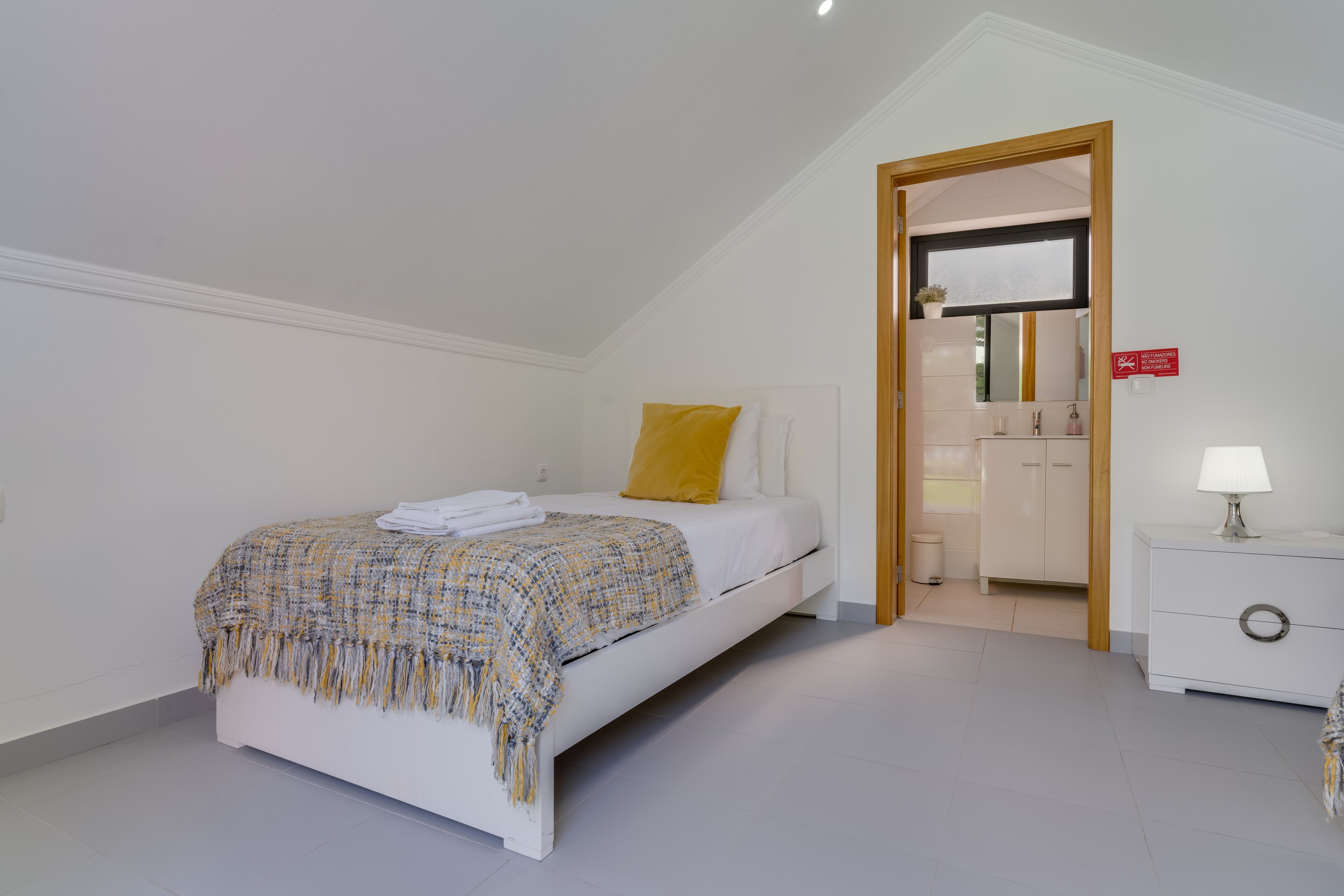 A bedroom with a bed, a bedside table, a nightstand, a mirror, and a door leading to a bathroom.