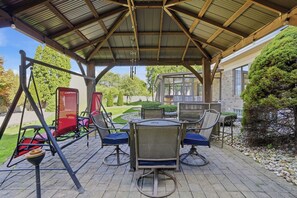 Un patio exterior con área de estar cubierta, que incluye un columpio y una mesa con sillas.