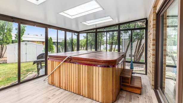 Un espace spa moderne doté d’un bain à remous en bois, de lucarnes et de grandes fenêtres offrant une vue sur le jardin arrière.