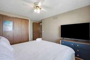 A bedroom with a bed, a ceiling fan, a wardrobe, a television, and a poster on the wall.
