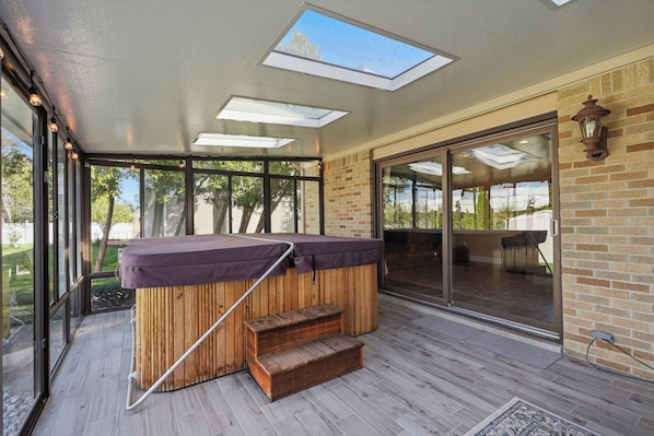 A hot tub with a wooden frame and steps, a glass door leading outside, and a skylight above.