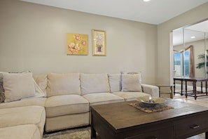 A living room with a beige sofa, a coffee table, and two framed floral paintings on the wall.